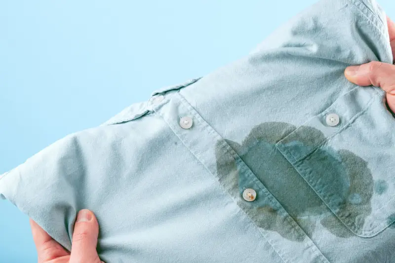 Person holding up blue shirt with a grease stain on it.