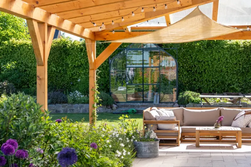 A covered patio in a sunny garden with outdoor furniture.