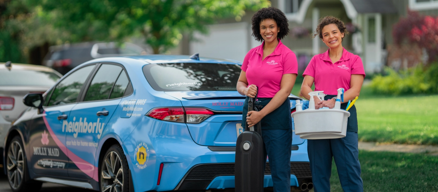 Molly Maid professionals standing beside a branded vehicle.