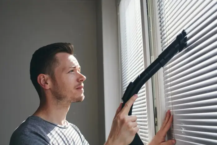 Man cleaning dust off blinds.