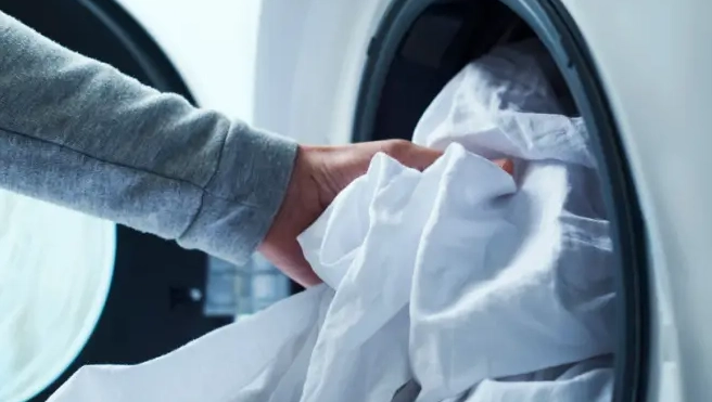 Person putting bedding into washing machine.