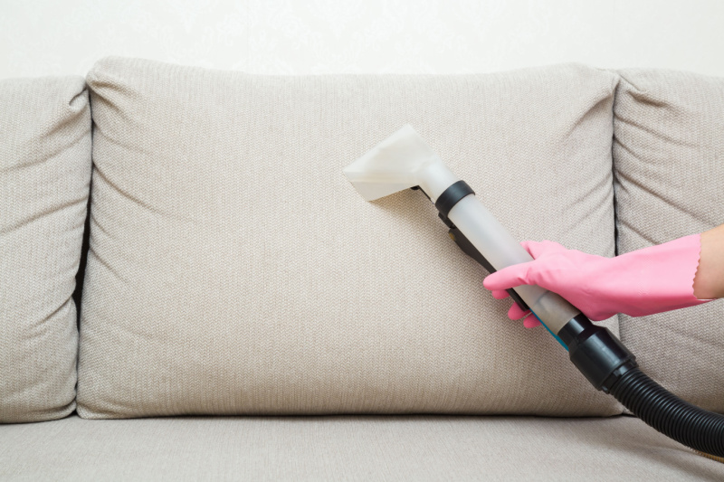 Person using vacuum on fabric couch.