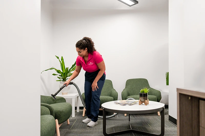 A Molly Maid professional vacuuming chairs in an office lobby 