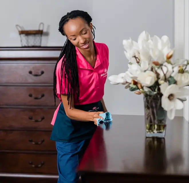 Molly Maid cleaning professional wiping a dresser in a bedroom.