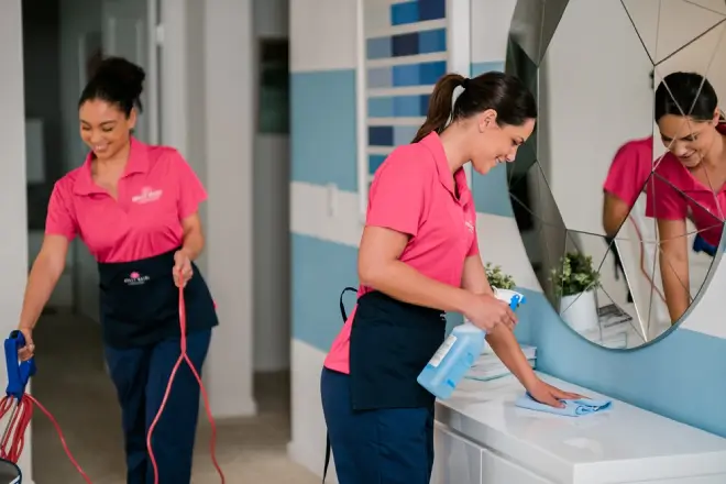 Molly Maid cleaning professionals vacuuming and wiping a dresser in a home. 