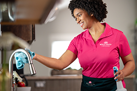 Molly Maid cleaning a kitchen sink faucet.