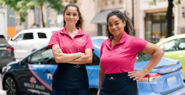 Two Molly Maids standing beside a branded car.