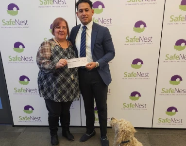 Two people holding a check with a dog sitting at their feet.