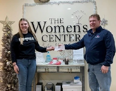 Two people holding a check in front of The Women's Center backdrop.