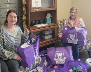 two women holding purple bags full of donated products.