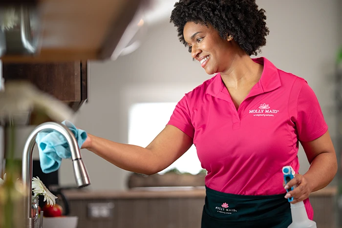 Molly Maid professional cleaning the sink in a kitchen. 