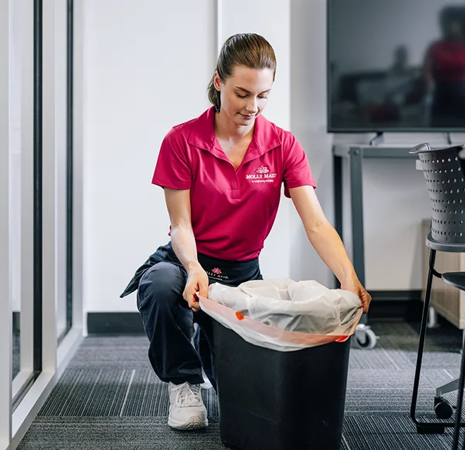 Molly Maid professional emptying the trash can at a business.