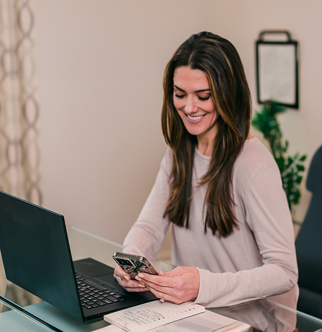 Smiling woman sitting at a desk looking at her mobile device.