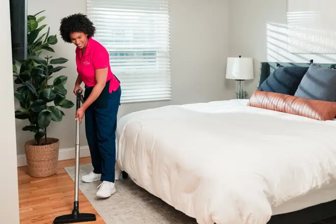 Molly Maid cleaning professional vacuuming a bedroom floor.