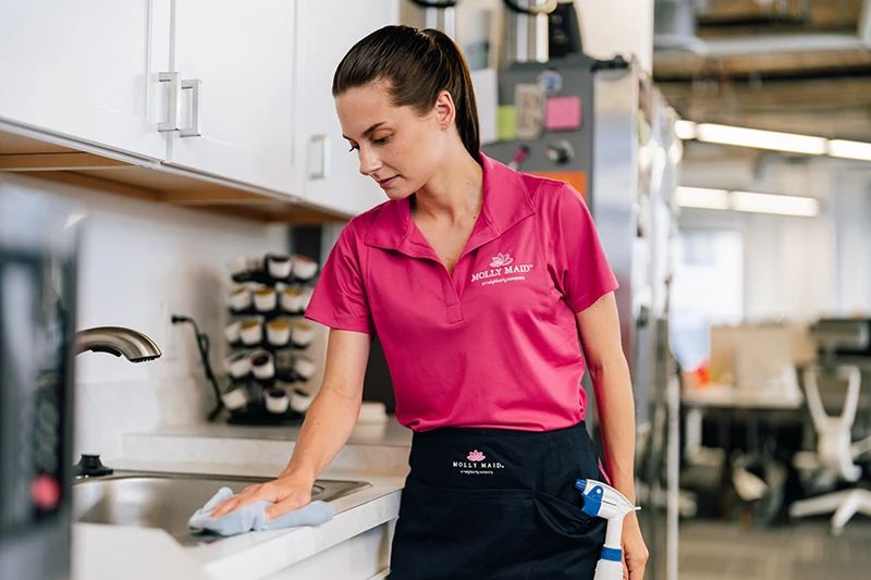 A Molly Maid service professional cleaning an office kitchen.