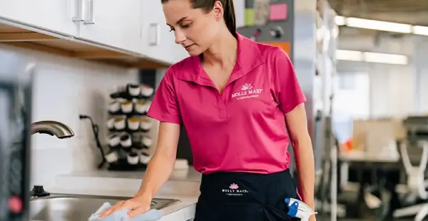 A Molly Maid professional cleaning an office kitchen.