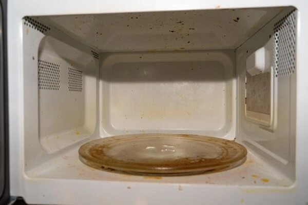 Inside view of a dirty microwave with cooking grease and food residue.