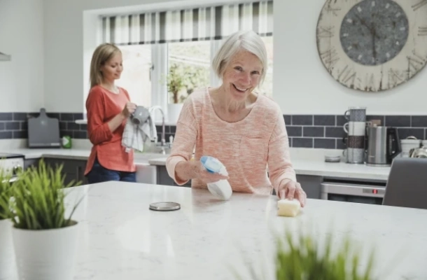 Elderly women cleaning kitchen counter with help from her daughter in the background