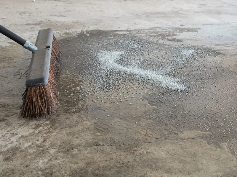 Person brushing cat litter on driveway grease stain