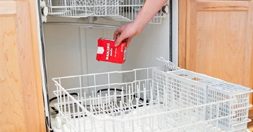 A person pouring baking soda into an empty dishwasher