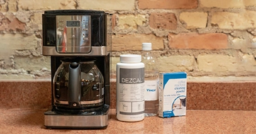 A coffee pot next to bottles of white vinegar and commercial descaler