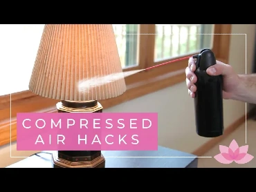 A person's hand spraying compressed air at the lampshade of a table lamp