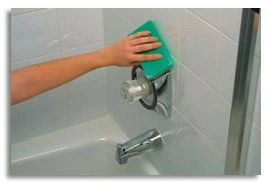 Hand cleaning a shower nozzle with a green sponge