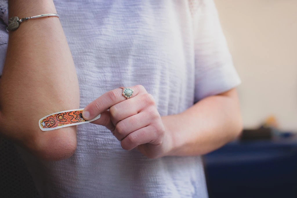 A person putting a brightly colored bandage on their elbow