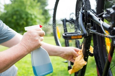 man using a spray bottle and yellow cloth to clean a bicycle.