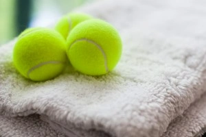 Three bright yellow tennis balls sitting on top of folded rugs