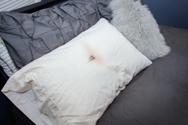 A white pillow on a bed with makeup stains on the pillowcase.