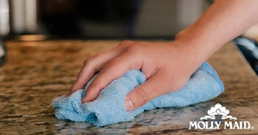 A hand cleaning granite countertop with a cloth.