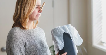 woman with clothespin on her nose looking into a trash can