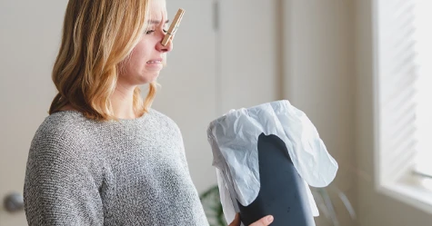 woman with clothespin on her nose looking into a trashcan