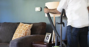 Person using a handheld hose vacuum on lampshade