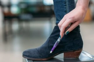 A person wearing a black suede boot and using a white pencil eraser on it