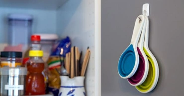 The interior of a kitchen cabinet with measuring spoons hung from a hook.