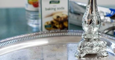 A silver platter with a silver candle holder on top, in front of a box of baking soda