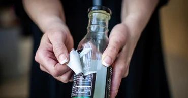 Hands removing sticker from a bottle