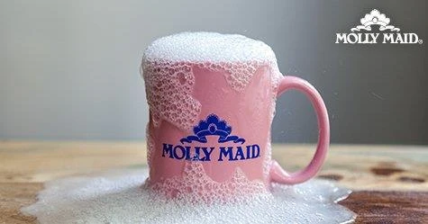 A sudsy pink coffee mug with the Molly Maid logo on a wood table.