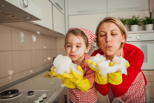 A mother and daughter wearing cleaning gloves and blowing on soapy suds.