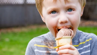 Little boy in a striped shirt eating chocolate ice cream out of a cone.