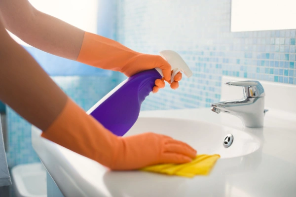 Person using spray bottle to clean bathroom sink