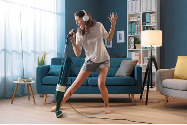 Cheerful woman cleaning up her home and singing, using the vacuum cleaner as a microphone.