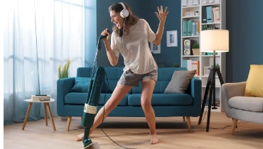 Cheerful woman cleaning up her home and singing, using the vacuum cleaner as a microphone.