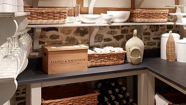 A well-organized kitchen pantry with open shelving showing jars, white ceramic containers, and baskets