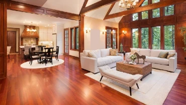 A grand living-dining area of a home with vaulted ceilings, wood beams, and rich hardwood floors throughout.