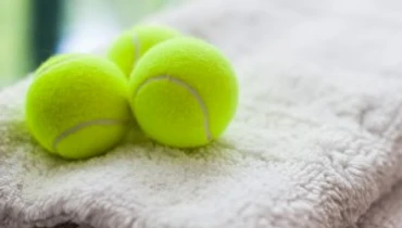 Three bright yellow tennis balls sitting on top of folded rugs