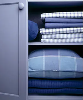 An open bureau showing neatly folded sheets and a pillow.