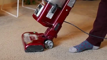 Person vacuuming carpet with a red vacuum